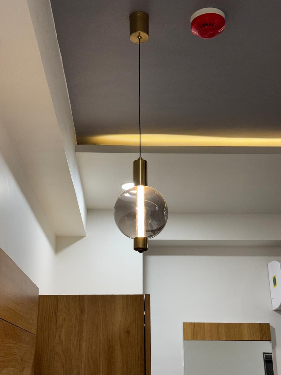 Une cuisine moderne avec un luminaire suspendu, des armoires en bois et un détecteur de fumée fixé au plafond.