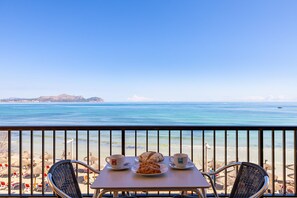 A balcony with a table set for two, overlooking a beach with umbrellas and lounge chairs. - Sol y Mar by Rentallorca (Can Picafort)