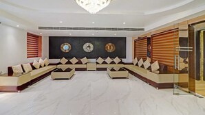 A modern living room with a sectional sofa, a chandelier, and decorative wall clocks. - Hotel Green View (Agra)