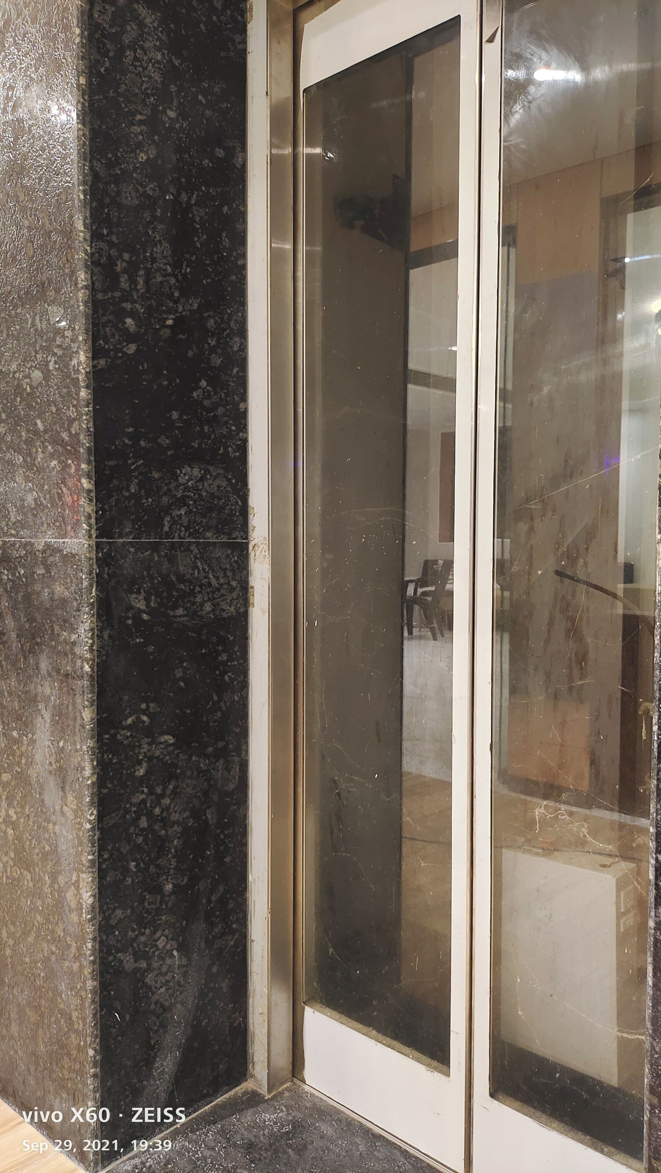 A corner of a room with a dark marble wall and a glass door.