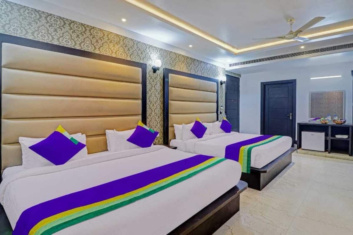 Habitación de hotel con dos camas, cada una con cabecero, un escritorio pequeño con silla y un ventilador de techo.