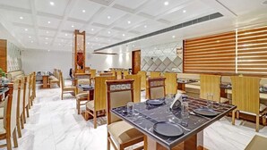 A modern dining area with marble flooring, wooden tables and chairs, and a high ceiling with recessed lighting. - Hotel Green View (Agra)