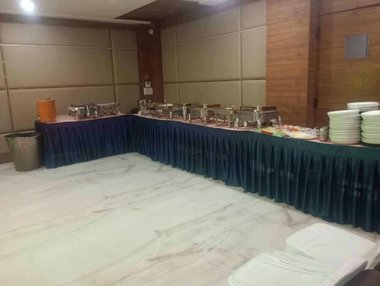 Un salón de banquetes con una larga mesa cubierta por un mantel azul, rodeada de sillas, y una pila de platos blancos a la derecha.