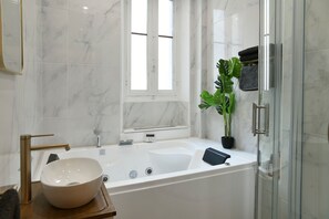 Une salle de bain moderne avec une grande baignoire, un mur en marbre blanc, une fenêtre et une plante en pot.