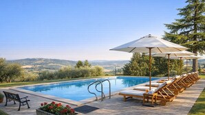 Una piscina con vista sulla campagna, sedie a sdraio e una panca.