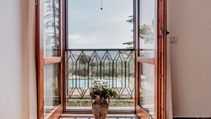 Vista attraverso una porta vetrata con ringhiera metallica, che conduce a una piscina e alla vegetazione.