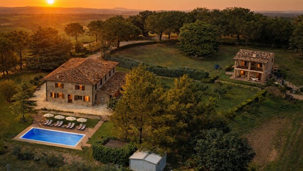 Un'ampia casa in pietra con piscina e area salotto esterna, circondata da alberi e un paesaggio collinare.