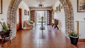 Un corridoio con un arco in mattoni, un lampadario, un divano e piante in vaso.