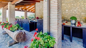 Una terrazza esterna con pareti in pietra, travi di legno, mobili in vimini e piante in vaso.