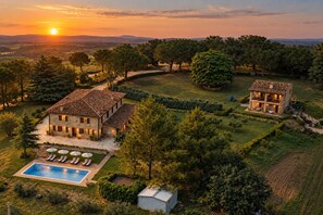 A large stone house with a swimming pool and outdoor seating, surrounded by trees and fields.