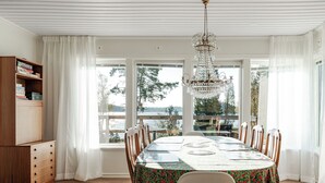 En spisestue med et stort bord, stole, en lysekrone og udsigt til en sø gennem store vinduer.