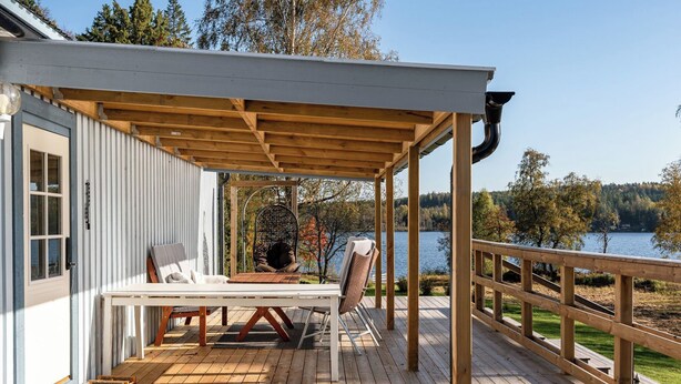 En træterrasse med et bord og stole, en hængekøjsstol og udsigt til en sø.