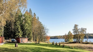 En hytte ved søen med en anløbsbro, omgivet af tætte træer og en græsplæne.