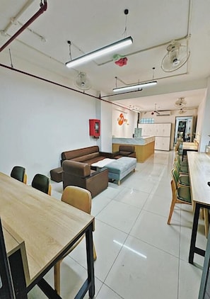 A modern room with a sofa, a dining table, and chairs. There is a kitchenette in the background.