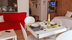Quarto de hotel moderno com área de refeições, sofá vermelho, televisão e uma garrafa de champanhe.