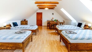Un dormitorio acogedor en el ático con cuatro camas dispuestas en forma de U, vigas de madera en el techo y un tragaluz.