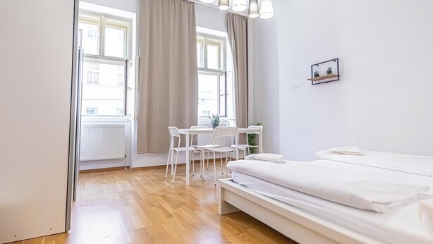 A bedroom with a bed, a desk, chairs, and a window with curtains. - Affordable Cozy 2BR Apt Near Stadthalle (Vienna)