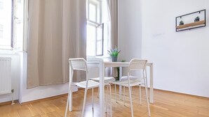 A room with a white table and four white chairs, a potted plant, and a framed picture on the wall. - Affordable Cozy 2BR Apt Near Stadthalle (Vienna)
