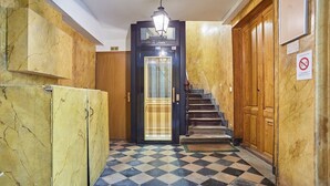 Ein Gang mit Schachbrettmuster, einer schwarze Tür mit Fensterglas und einer Holztreppe.