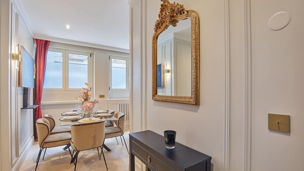 A dining area with a table set for four, a large ornate mirror, and a console table with a black object on it. - Eiffel Tower Apartment Invalides (Paris)