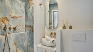 A bathroom with marble walls, a round mirror, a white sink, and a towel rack. - Eiffel Tower Apartment Invalides (Paris)