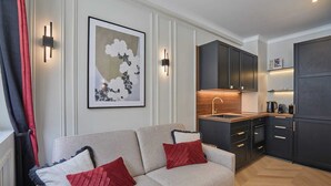 A modern living room with a sofa, a kitchen area with dark cabinets and a wooden countertop, and wall-mounted light fixtures. - Eiffel Tower Apartment Invalides (Paris)