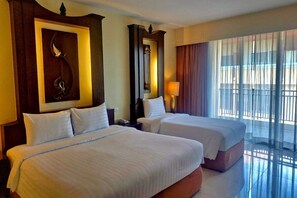 Une chambre d’hôtel avec deux lits, un grand miroir, un élément décoratif mural, une lampe et une vue sur l’extérieur à travers des rideaux transparents.