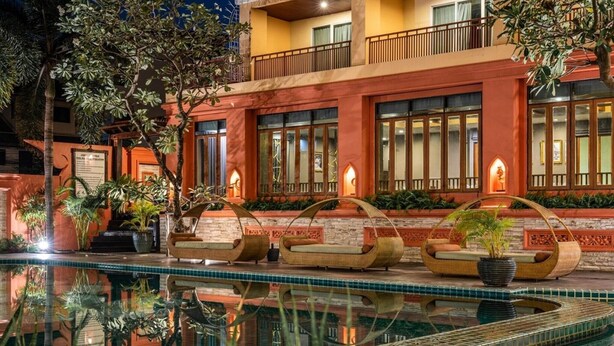 Un hotel con piscina, mobiliario exterior e iluminación en la fachada.