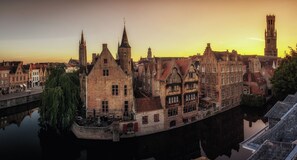 Un pueblo histórico europeo con una imponente torre de iglesia y un canal que refleja los edificios.
