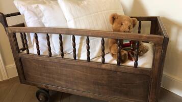 Una cuna de madera con un oso dentro, ruedas y almohadas blancas.