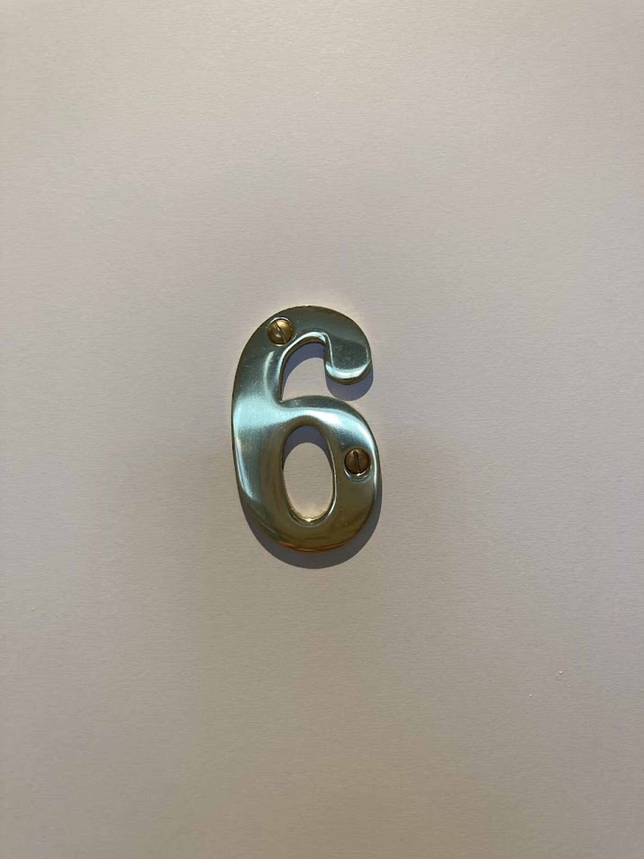 A metallic number 6 on a plain wall.