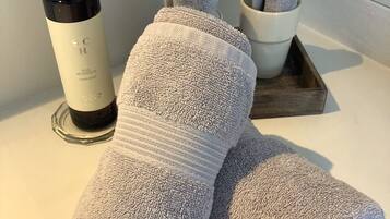 A bathroom with a white sink, a bottle of hand soap, and two rolled towels.