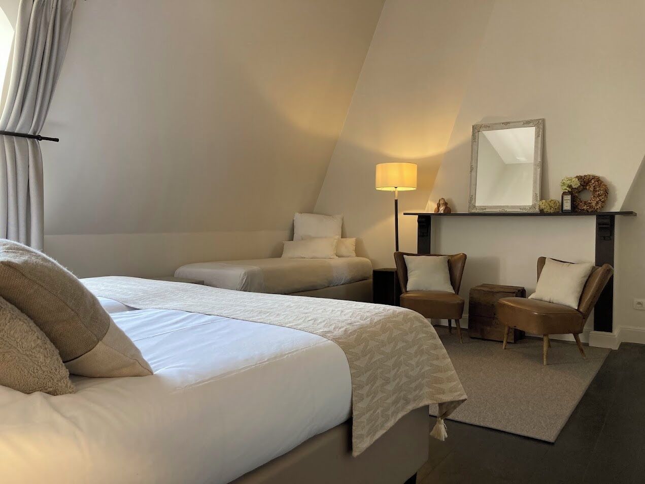 A hotel room with two beds, a sitting area with chairs, a lamp, and a mirror on the wall.