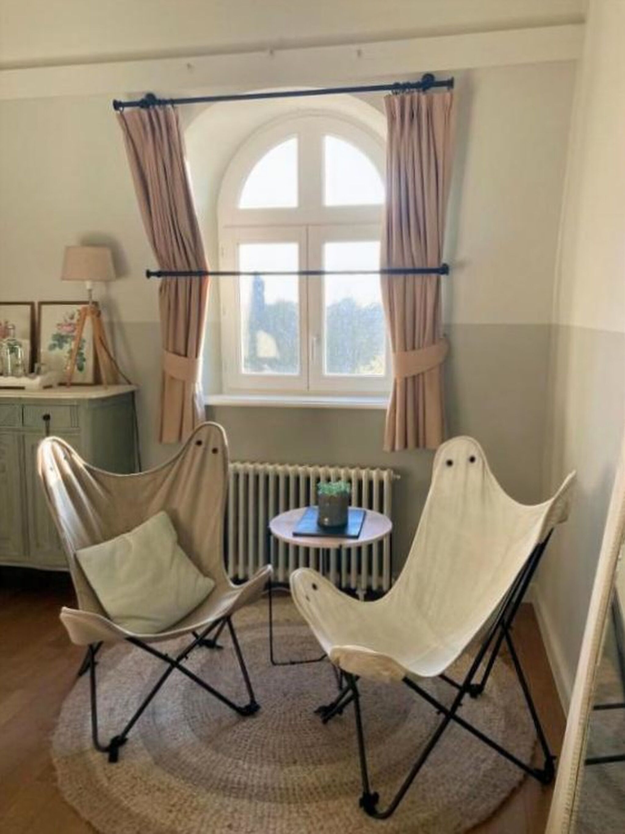 A room with two chairs, a small table, a radiator, and a window with curtains.
