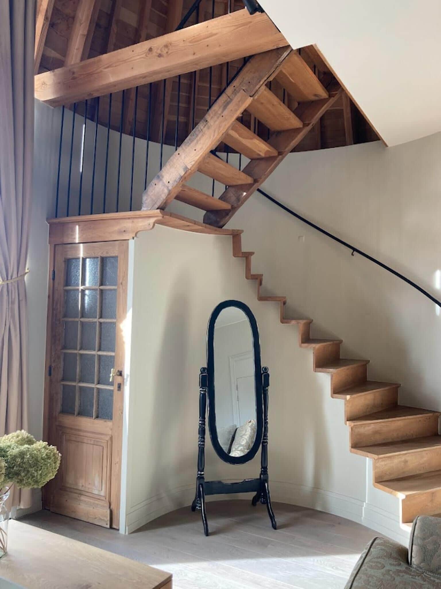 Un escalier avec des marches en bois et une rampe en bois, menant à une mezzanine dont les poutres apparentes sont visibles.
