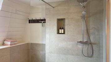 Una ducha moderna con puerta de cristal, un perchero y un estante pequeño con botellas.