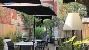 An outdoor patio area with brick flooring, tables, chairs, and umbrellas providing shade. - Chateau Fort Lapin (Bruges)