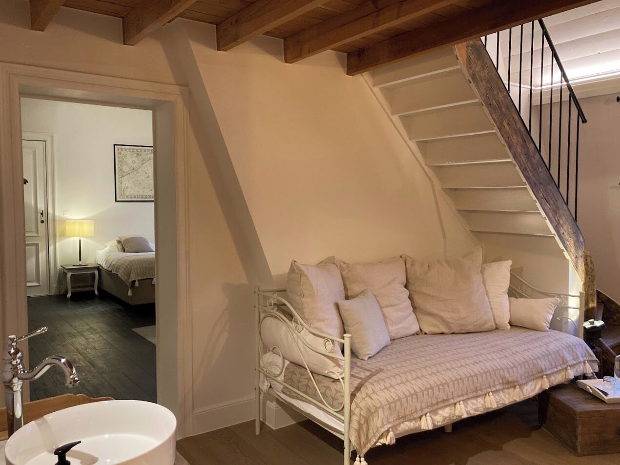 A cozy bedroom with a bed, a bedside table, a lamp, and a view of a staircase.