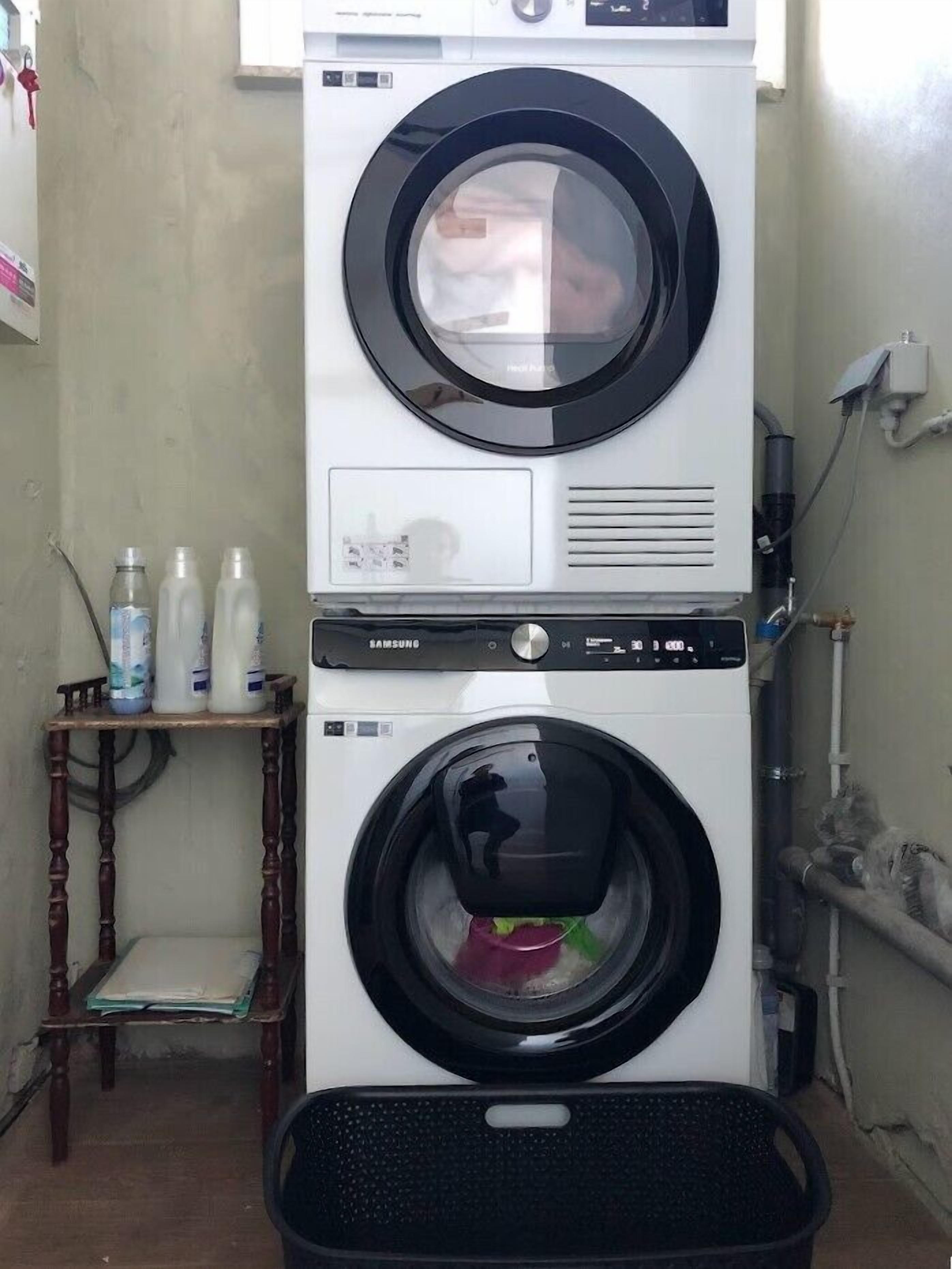 Een gestapelde wasmachine en droger met een houten tafel en flessen wasmiddel in de buurt.