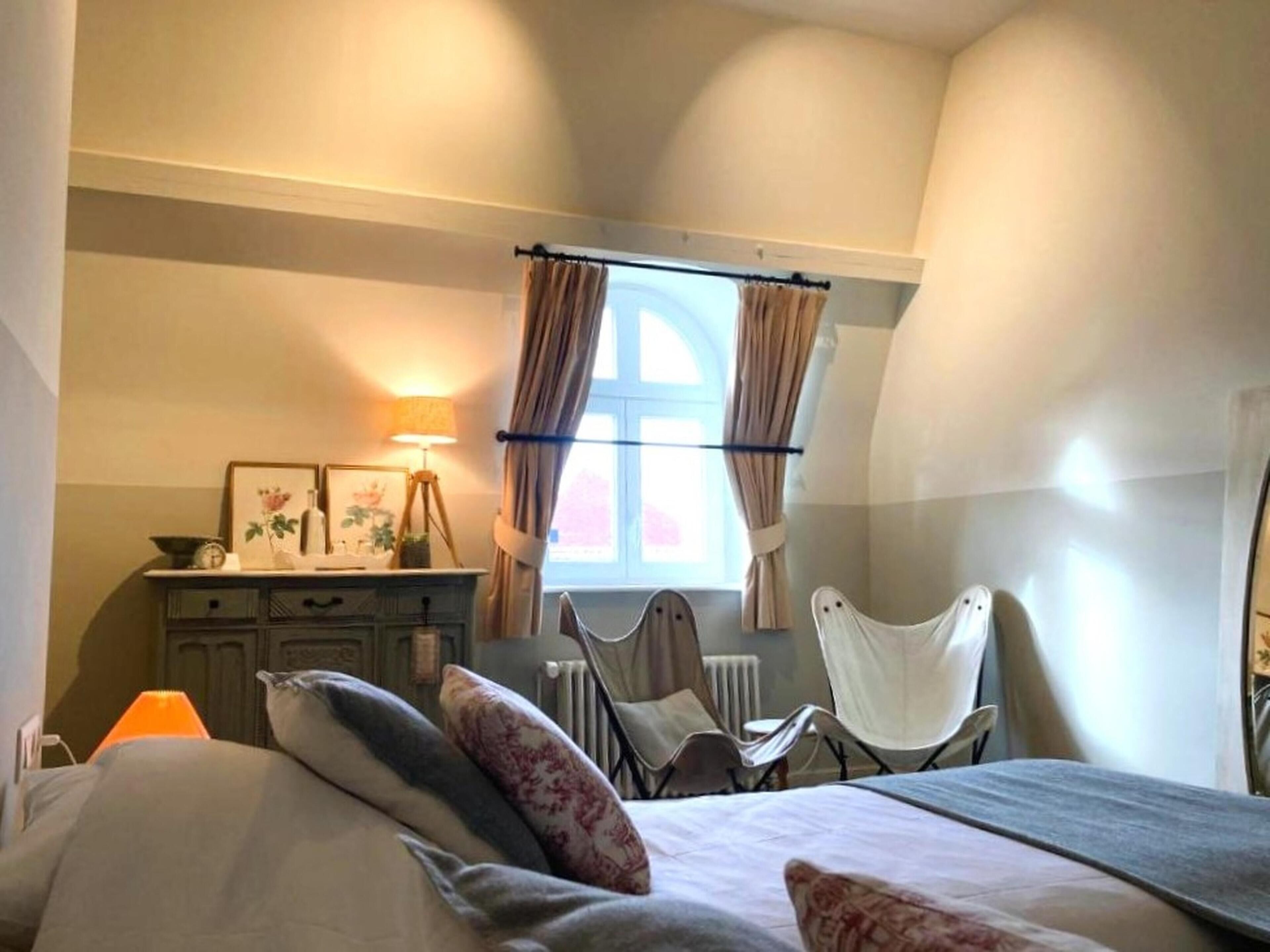 Een slaapkamer met een bed, een bureau, een stoel en een raam met gordijnen.
