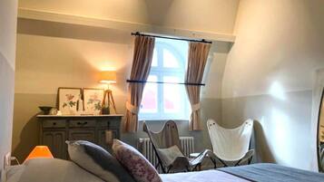 Een slaapkamer met een bed, een bureau, een stoel en een raam met gordijnen.
