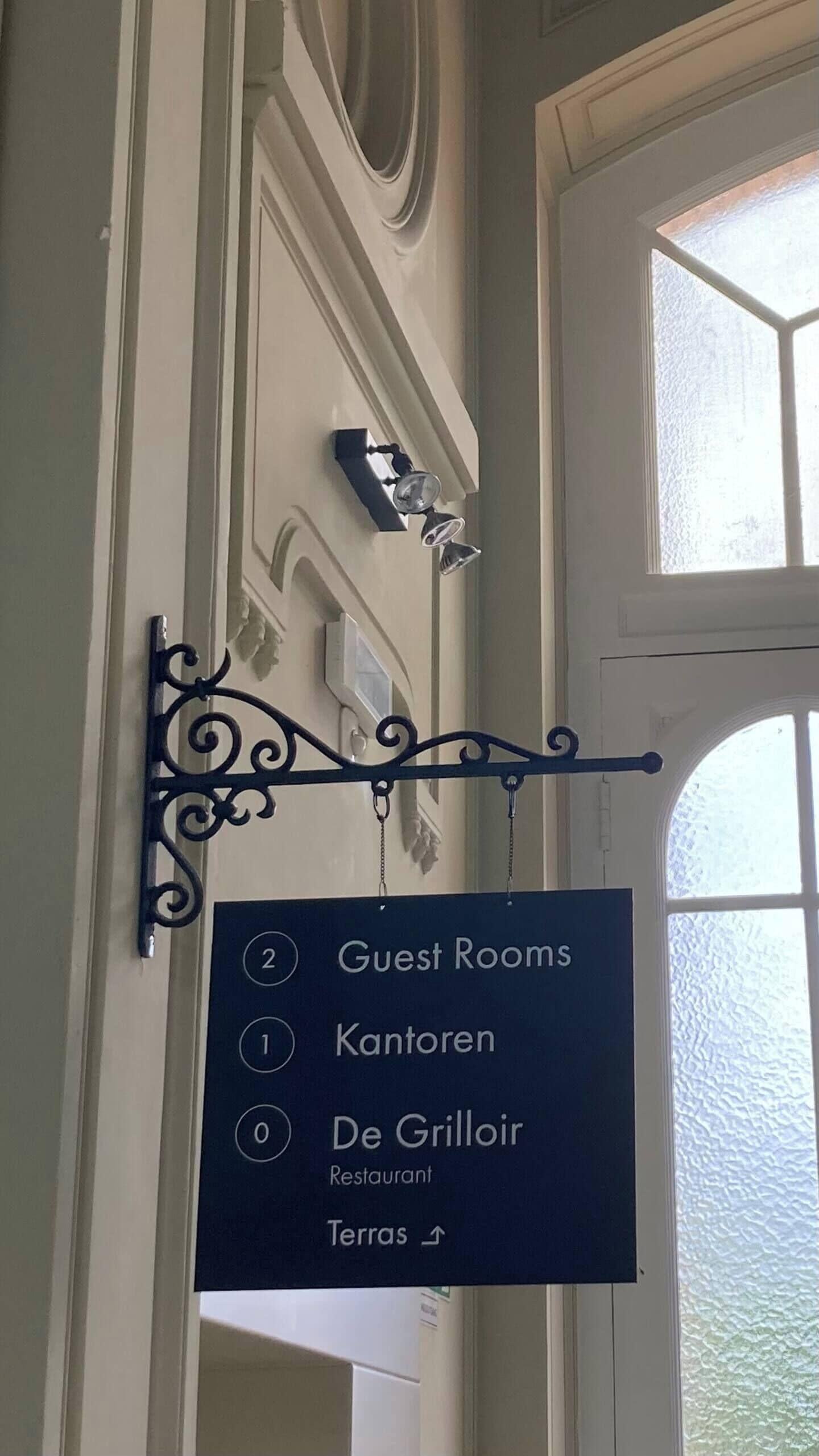 Ein Schild mit Zimmernummern und -bezeichnungen, das Gästezimmer, eine Kantorei, ein Restaurant und eine Terrasse ausweist.