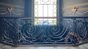 A balcony with ornate wrought iron railings and a large arched window with a stained glass design. - Chateau Fort Lapin (Bruges)
