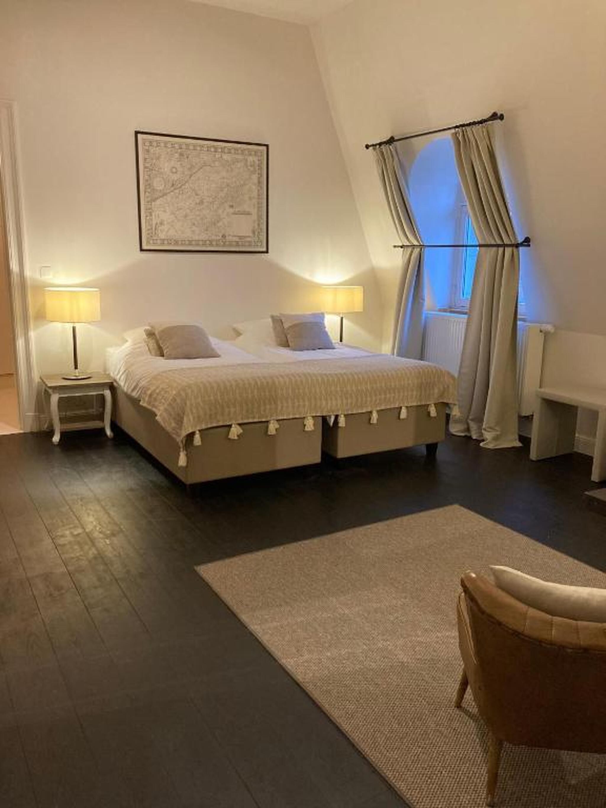 A bedroom with a large bed, two bedside tables with lamps, a rug, and a chair.