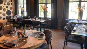 A restaurant interior with round tables, dark chairs, and large windows with curtains. - Chateau Fort Lapin (Bruges)