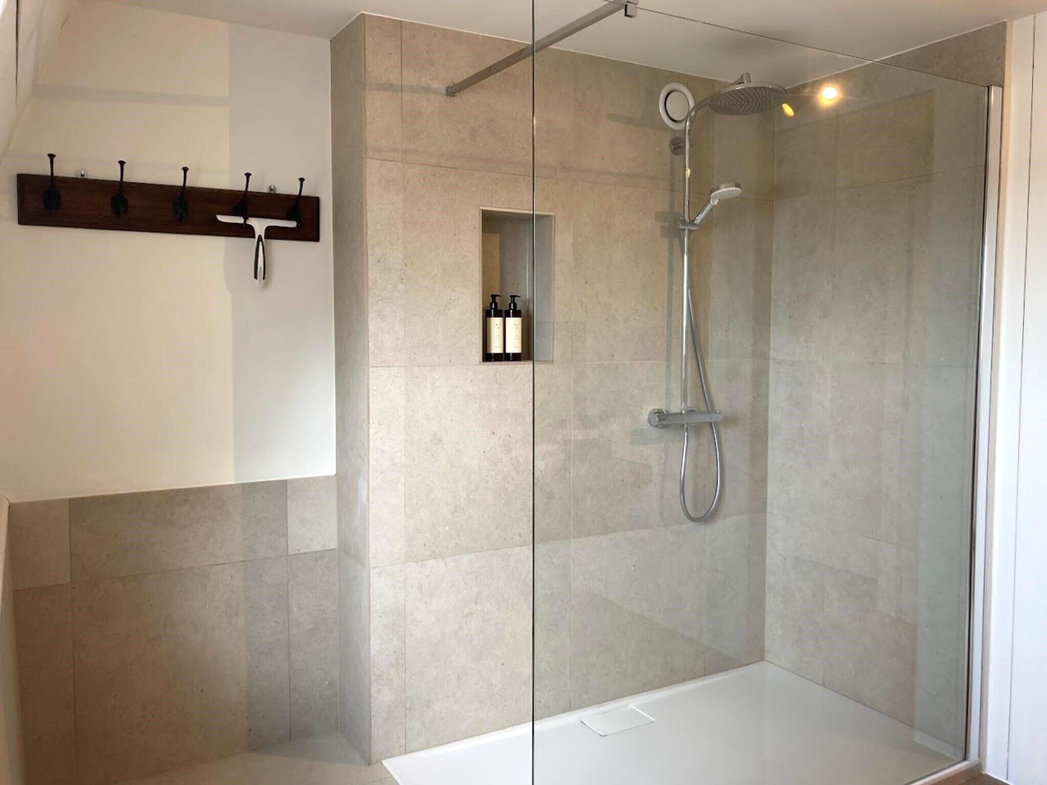 Un área de ducha moderna con puerta de cristal, cabezal de ducha de mano y un estante pequeño con botellas.