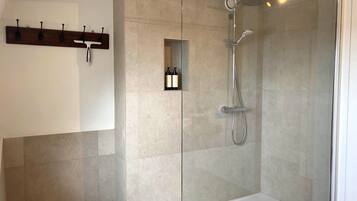 Un área de ducha moderna con puerta de cristal, cabezal de ducha de mano y un estante pequeño con botellas.