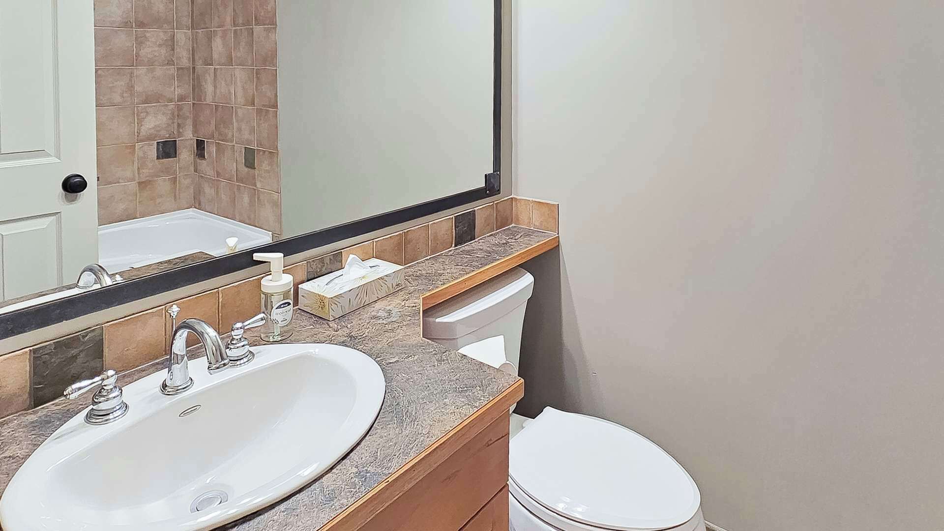 A bathroom with a white sink, a mirror, a toilet, and a towel dispenser.