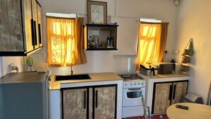Eine kleine Küche mit Gasherd, Backofen und Spüle. Auf der Arbeitsfläche steht eine Mikrowelle, und es gibt einen kleinen Tisch mit Stühlen.