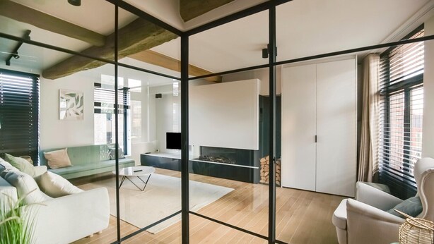 Un salon moderne avec une cloison en verre, un plancher en bois, un canapé, un fauteuil et une cheminée.
